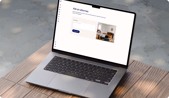 Laptop on wooden floor displaying a webpage with an 'Ask an attorney' section and a photo of two people sitting on a couch.