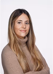 Smiling young woman with long light brown hair wearing a brown turtleneck sweater against a white background.