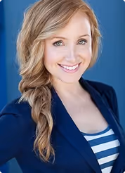 Smiling woman with long blonde braided hair, wearing a navy blazer over a striped shirt, against a blue background.