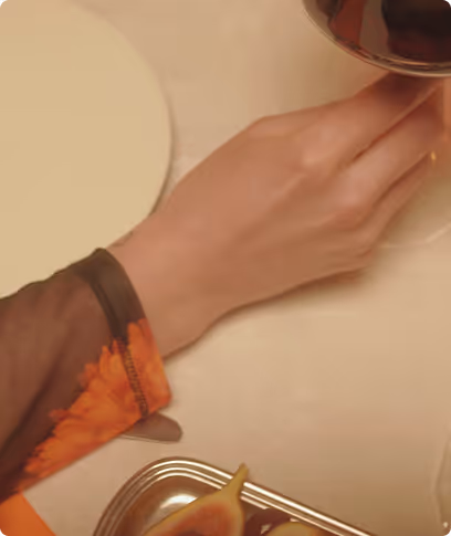 Hand holding a glass of red wine over a table with fruit and a plate.