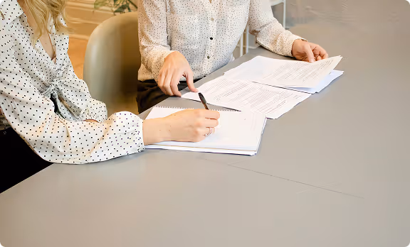 Two people reviewing and signing documents at a gray table.