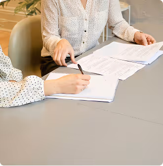 Two people reviewing and signing documents at a gray table in an office setting.