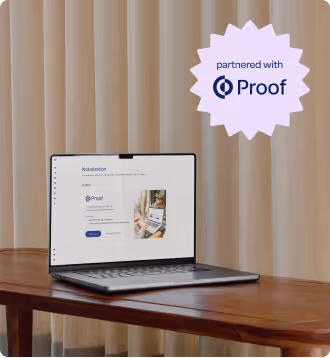 Open laptop on wooden table displaying a website page with Proof branding and a pink starburst graphic saying 'partnered with Proof' on beige curtain background.