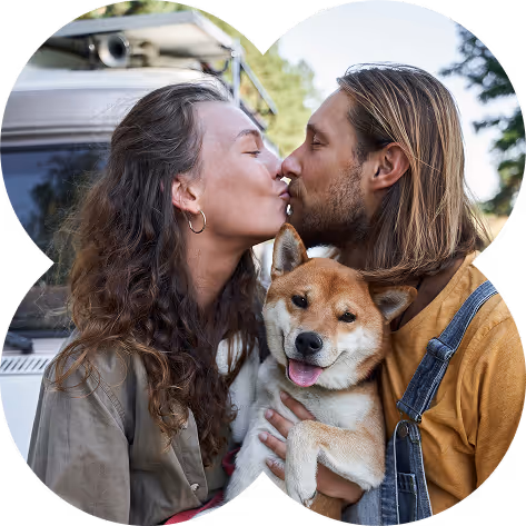Couple kissing while holding a smiling Shiba Inu dog outdoors near a vehicle.