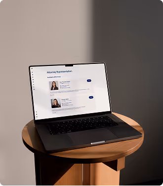 Open laptop on a round wooden table displaying an attorney representation webpage with photos and names of two female lawyers.