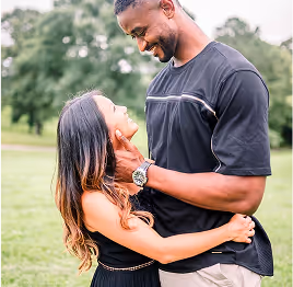 Couple embracing and looking lovingly at each other outdoors in a grassy park.