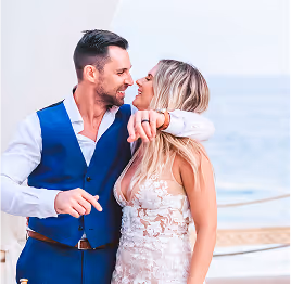 Bride and groom smiling and embracing each other outdoors by the water.