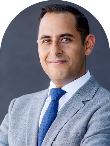 Confident man in gray suit and blue tie smiling against a dark gray background.