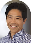 Smiling man with short black hair wearing a checkered shirt against a white background.