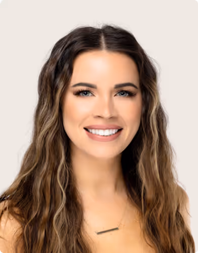 Smiling woman with long wavy brown hair and blue eyes against a light background.