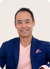 Smiling man in a navy blazer and pink shirt with a pink pocket square against a light background.