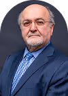 Portrait of an older man with glasses, a beard, and a mustache wearing a blue suit and checkered blue tie.