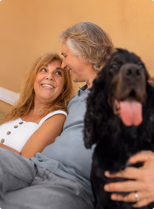 Smiling middle-aged couple sitting close together with a large black dog in the foreground.