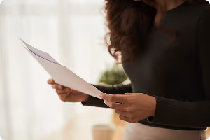 Person holding and reading a sheet of paper indoors with soft natural light.