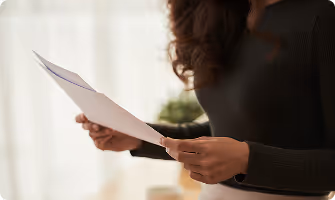 Person with dark curly hair wearing a black long-sleeve shirt holding a white sheet of paper.