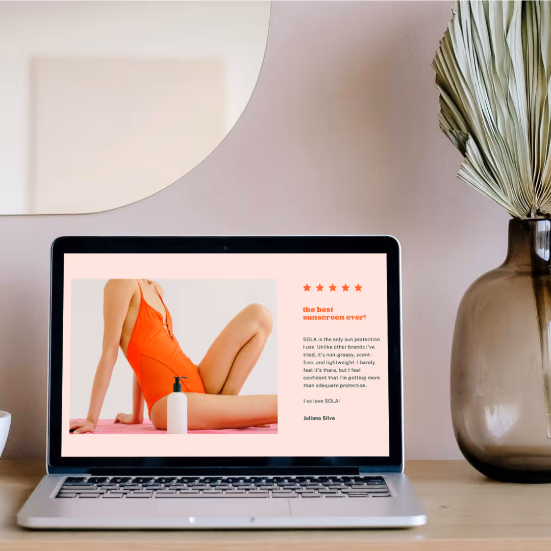 Laptop on wooden desk displaying a skincare product review featuring a person in an orange swimsuit and a sunscreen bottle, with a large vase and dried leaves nearby.