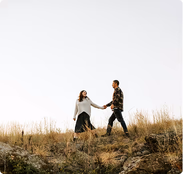 Couple holding hands and walking on a grassy hill under a clear sky.