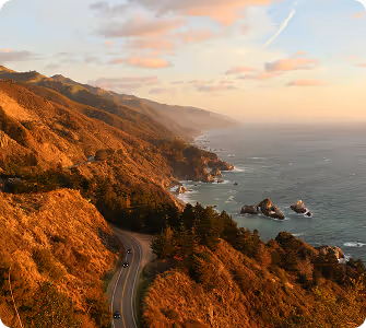 Coastal highway winding along rugged cliffs and ocean at sunset with scattered clouds.