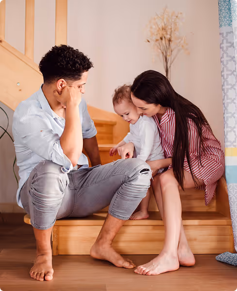 A family with a man, woman, and baby sitting on wooden stairs, smiling and interacting closely.