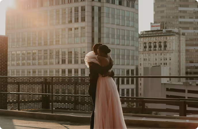 Couple embracing on a rooftop terrace with city buildings in the background at sunset.