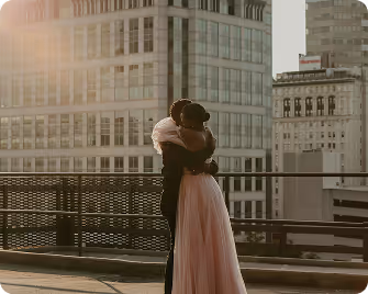 Couple embracing on a rooftop with tall city buildings in the background at sunset.