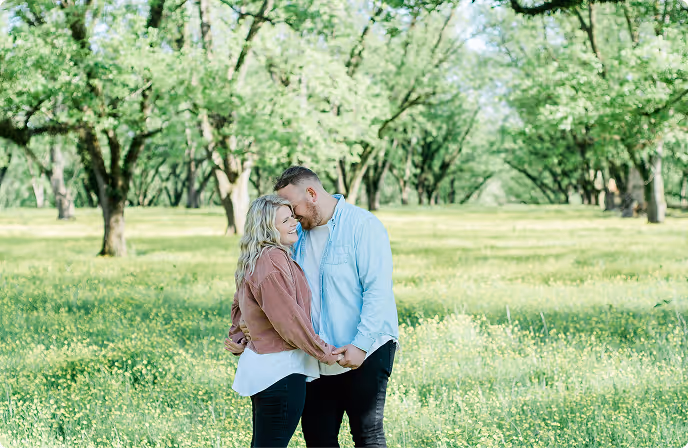 Couple holding hands and embracing in a sunlit green orchard.