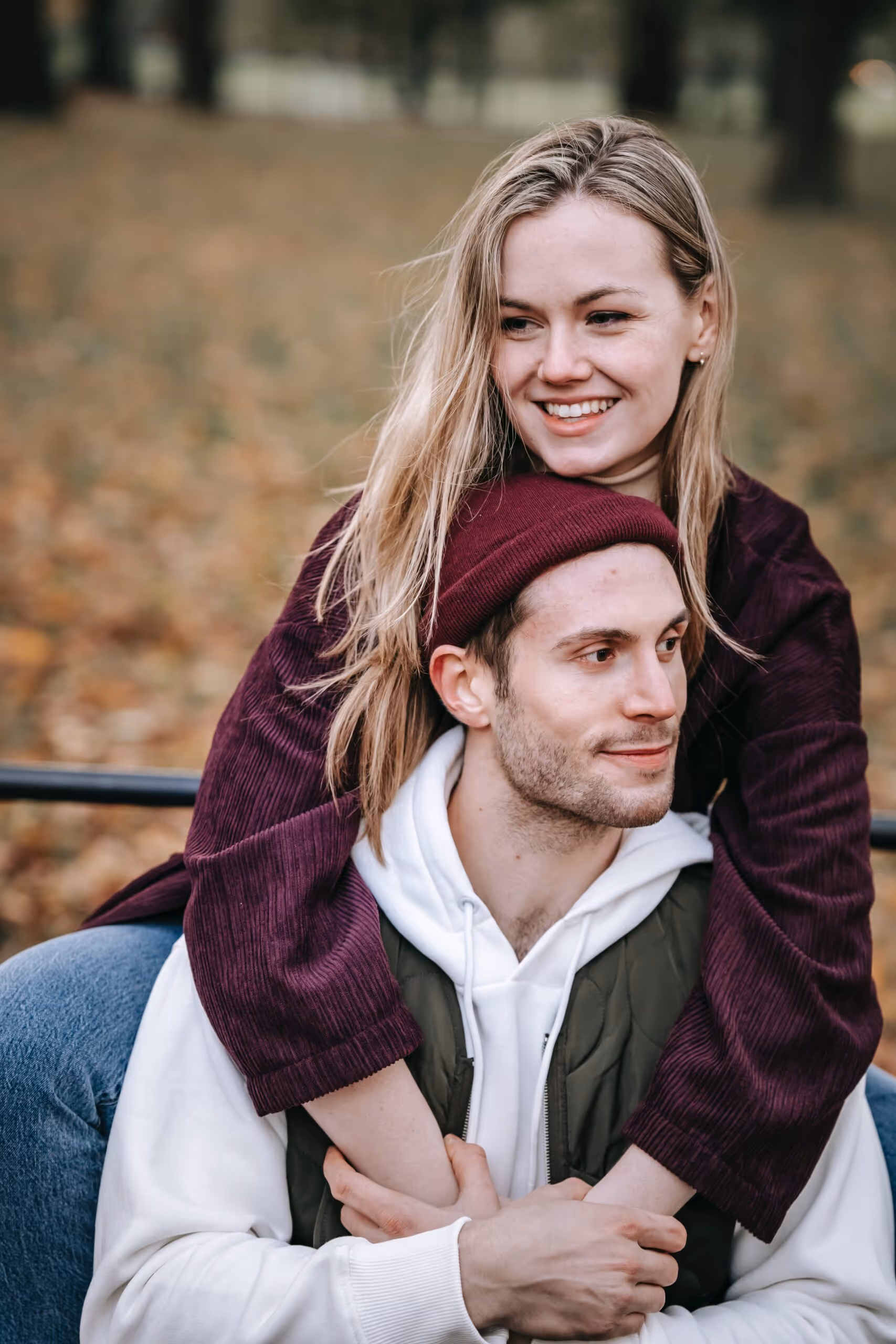 Smiling woman hugging a man from behind outdoors in autumn.