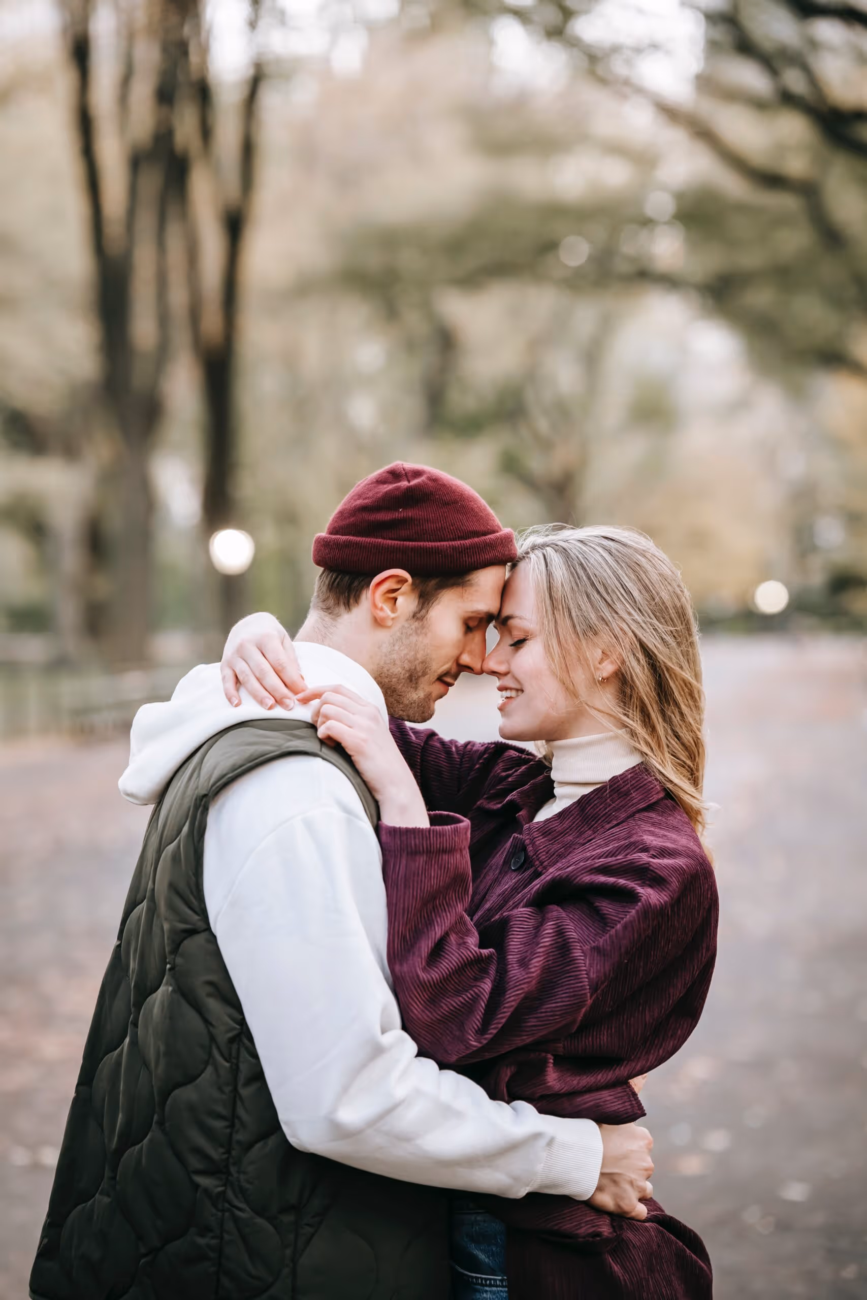 Young couple embracing with their foreheads touching outdoors on a blurred tree-lined path.
