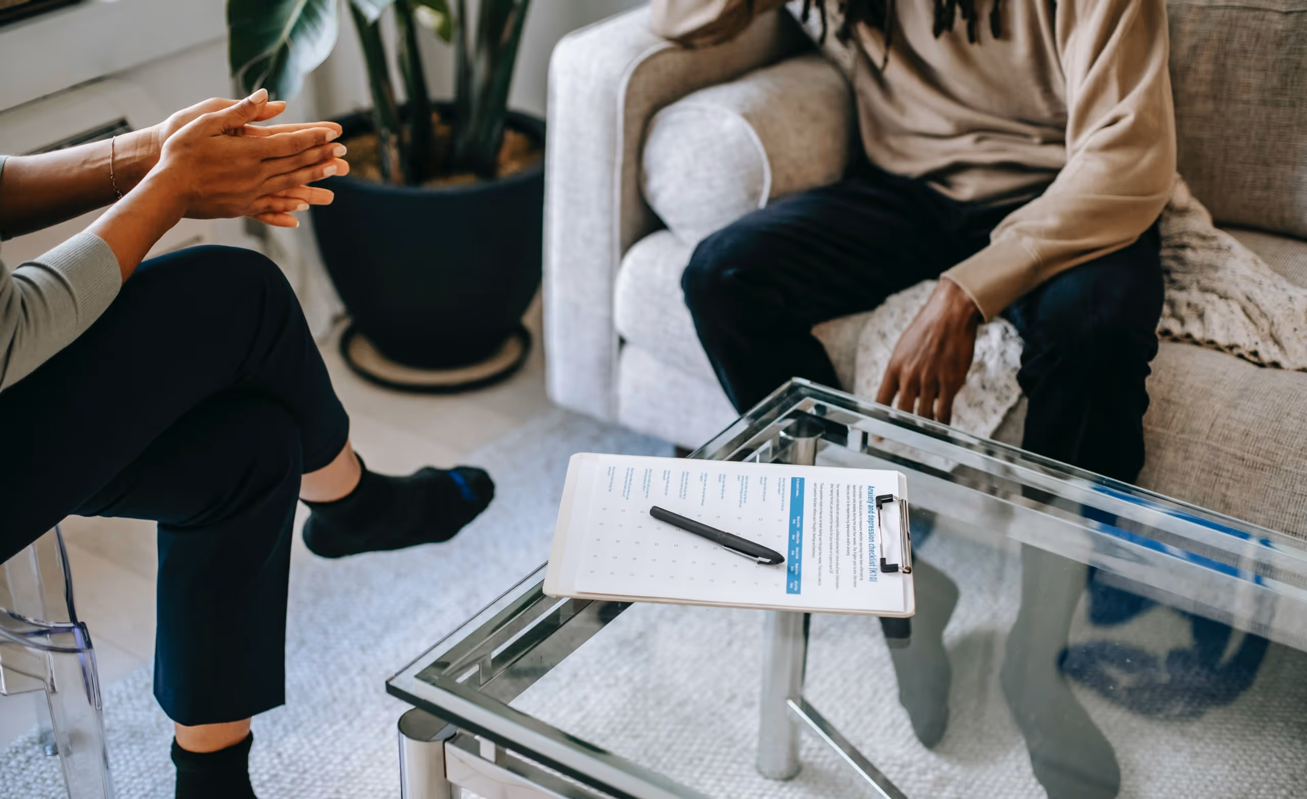 Two people having a discussion in a living room with a clipboard and pen on a glass coffee table between them.
