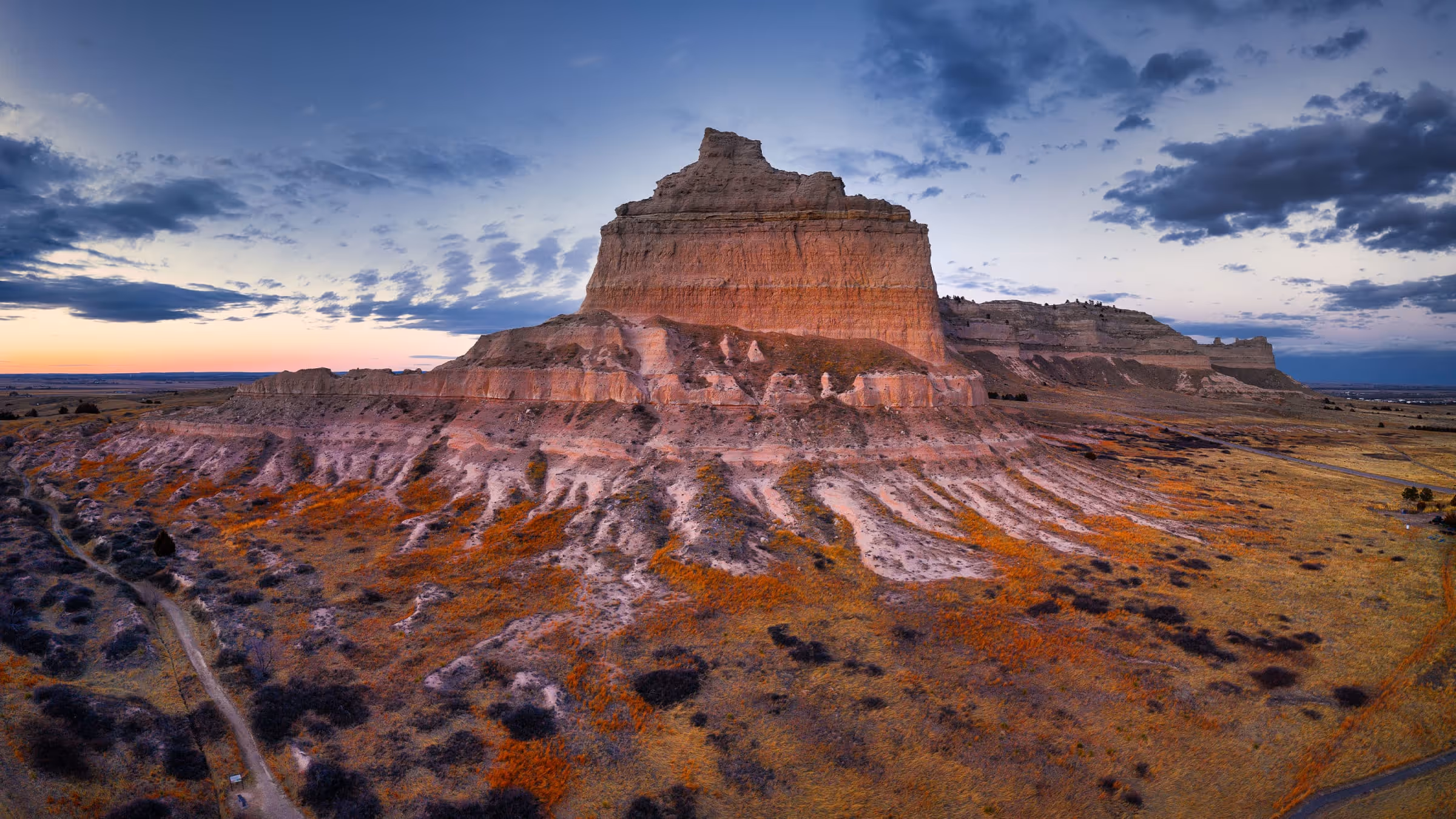 Butte formation in a colorful landscape under a partly cloudy sky at sunset.