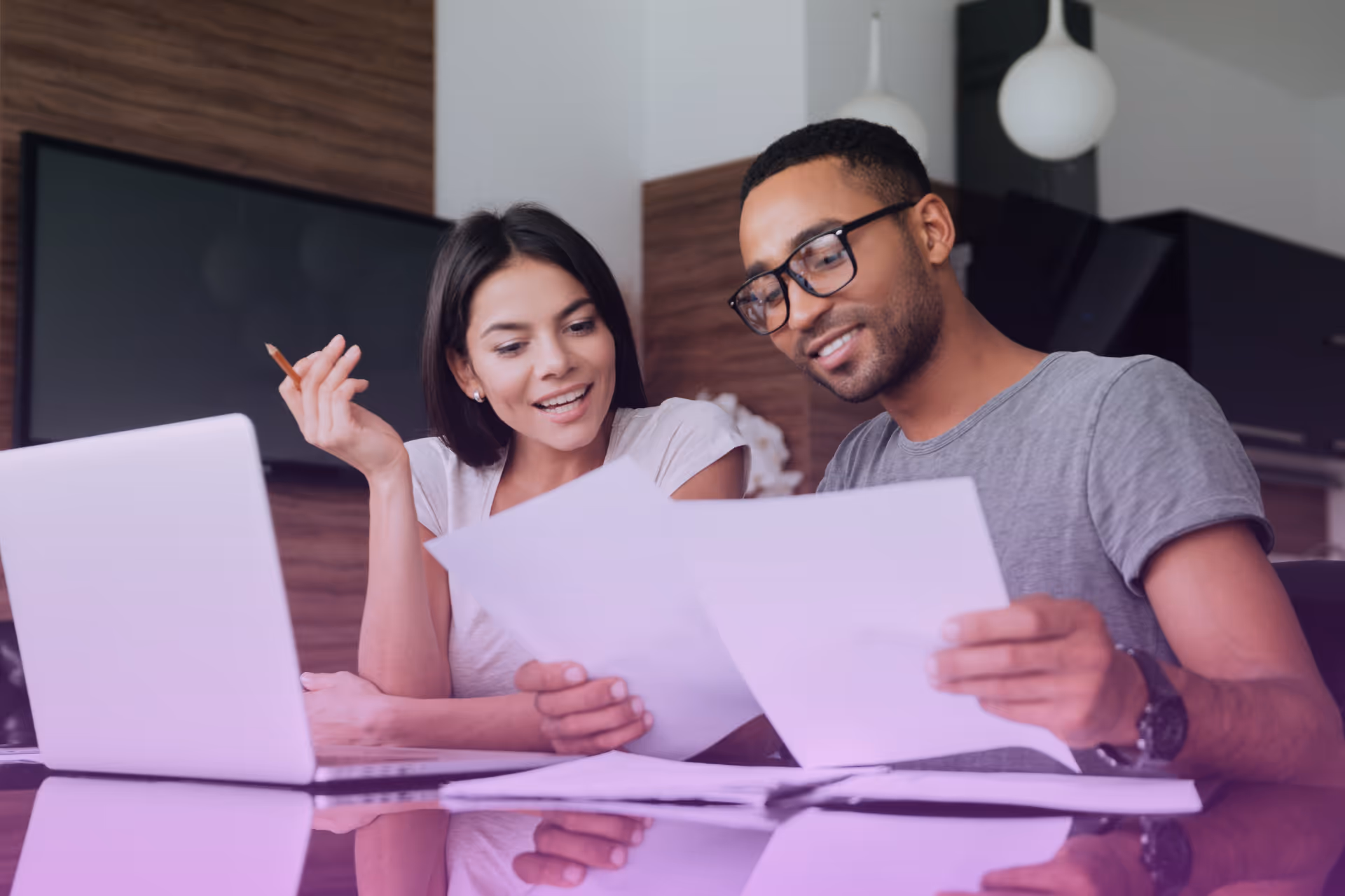 Couple sitting at a table reviewing documents together with a laptop nearby.