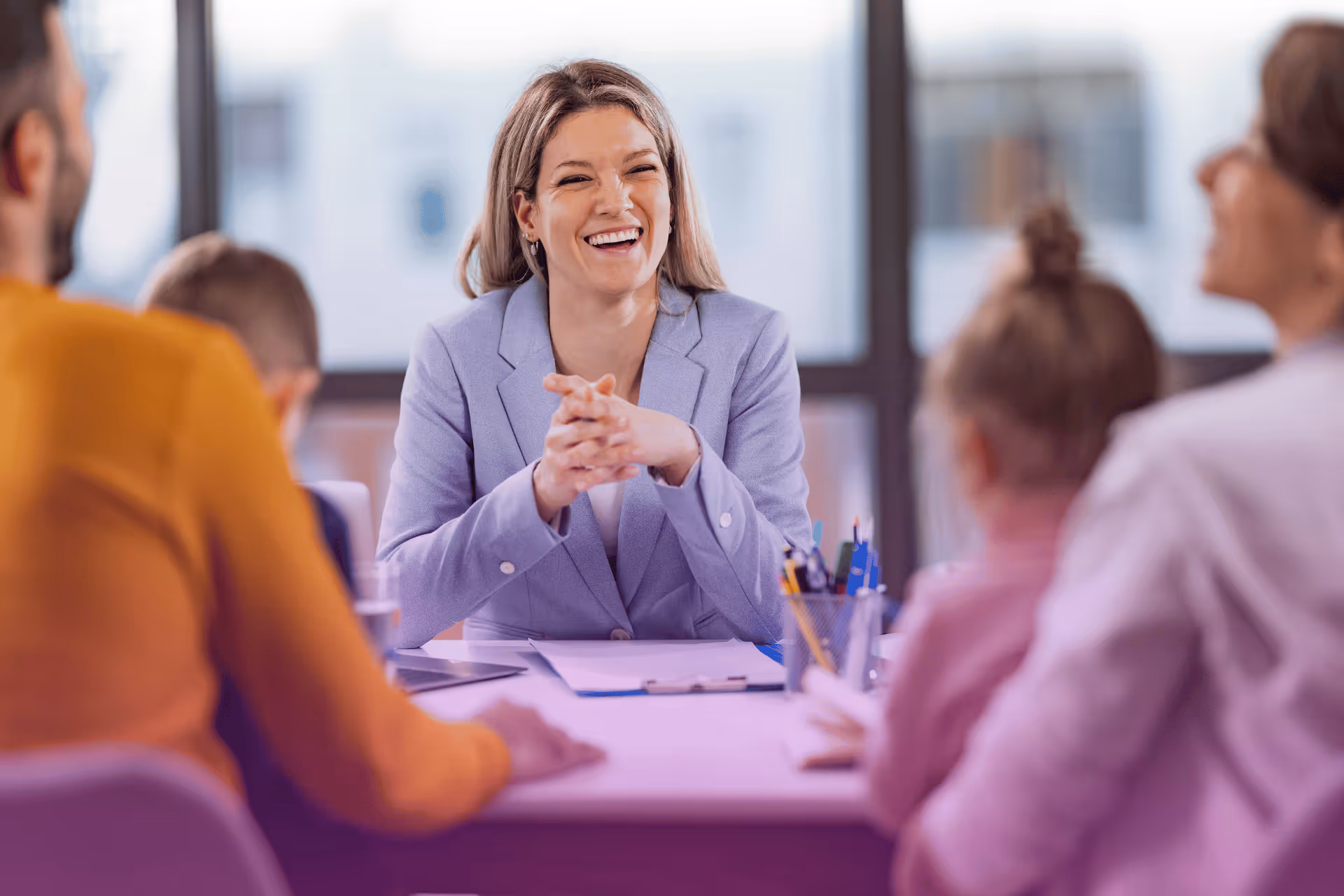 Smiling female lawyer in a light purple blazer talks to a family of four at a desk in a bright office.