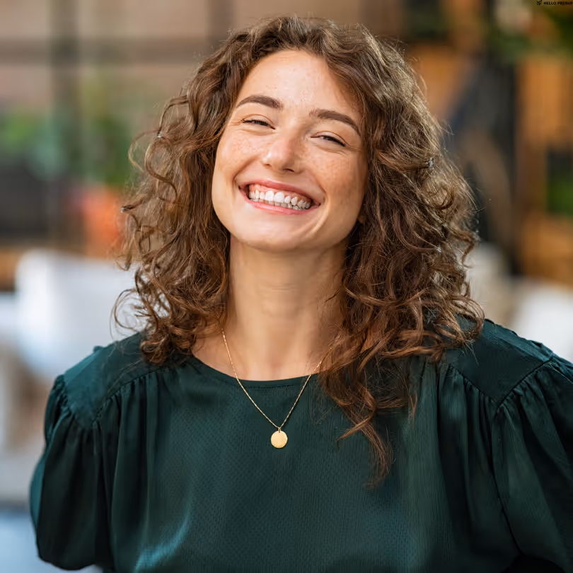 Smiling woman with curly brown hair wearing a dark green blouse and a gold necklace.