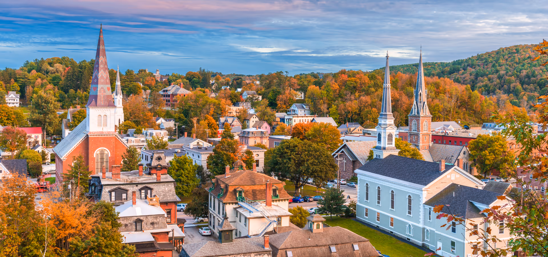 Aerial view of a small town with colorful autumn trees surrounding historic buildings and churches with steeples.