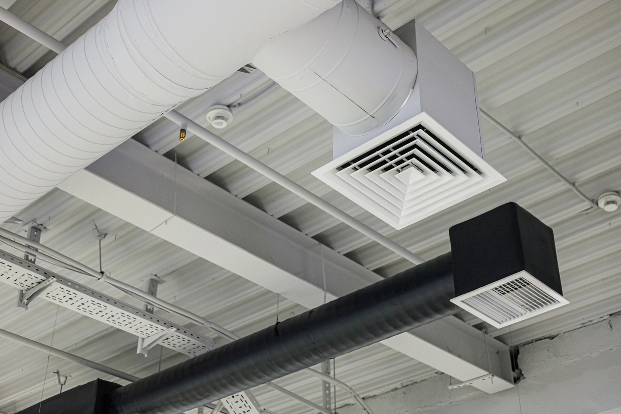 Ceiling with industrial air ducts and vents; white duct with a square vent and a black duct with a rectangular vent.