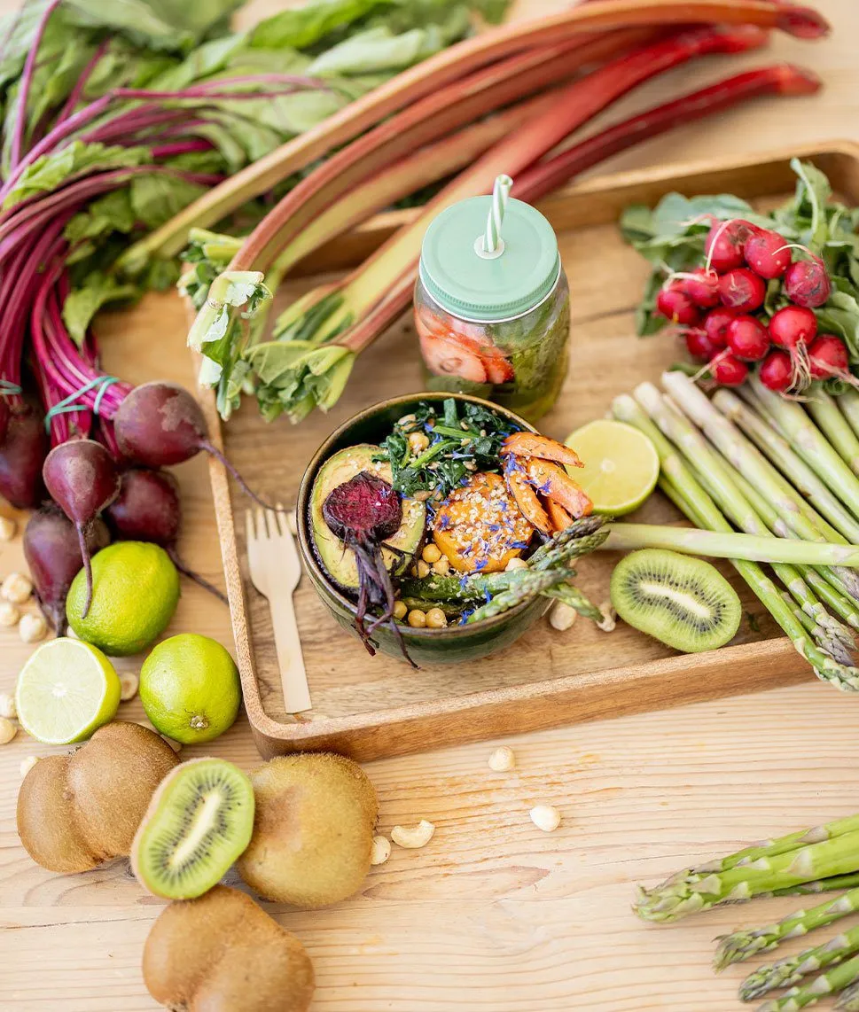 Assorted healthy foods including avocados, tomatoes, leafy greens, nuts, grains, and fruit arranged on a table.