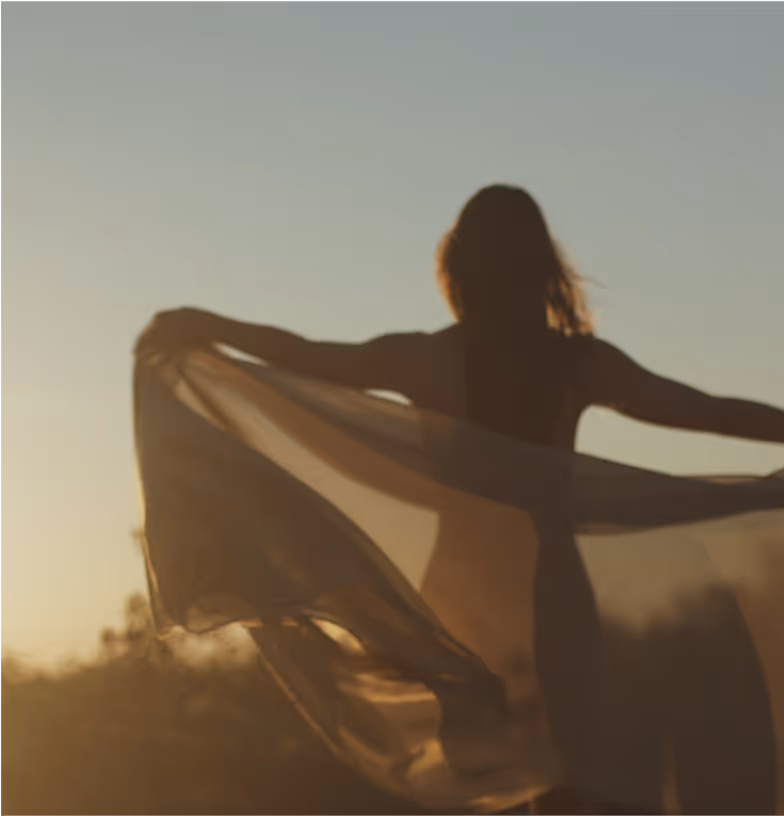 Woman at sunrise holding a scarf blowing in the breeze.