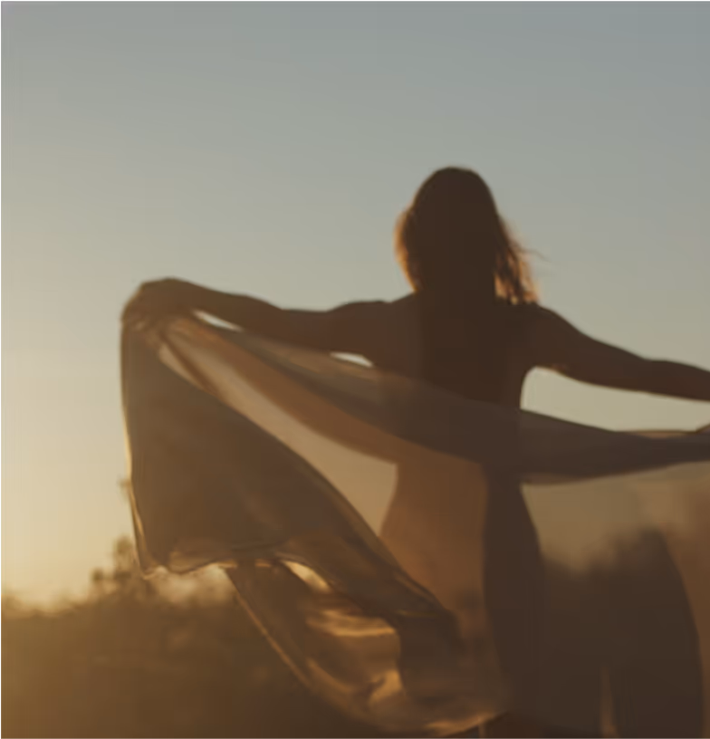 Woman at sunrise holding a scarf blowing in the breeze.