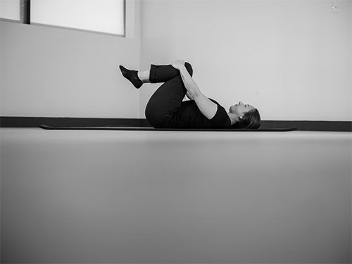 Woman lying on your back, take hold of both legs behind the knees and pull them gently in toward her chest.