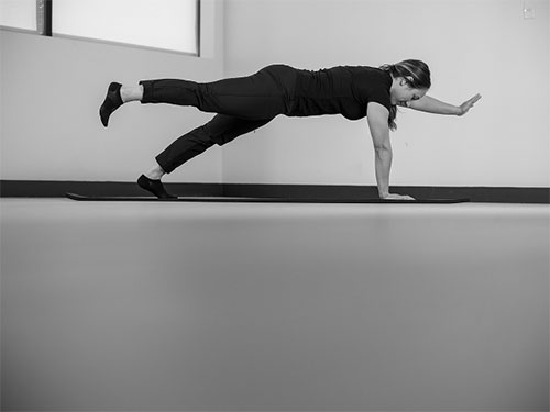 Woman performing a plank, on hands and toes, raise one arm and the opposite leg.