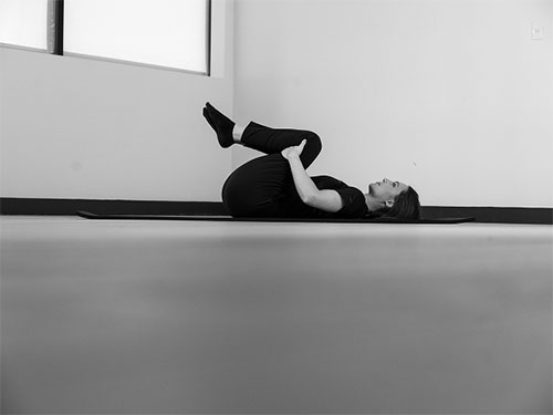 Woman lying on your back, take hold of both legs behind the knees and pull them gently in toward her chest.