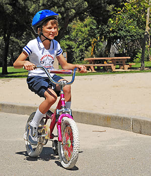 Child wearing helmet riding bicycle in park.