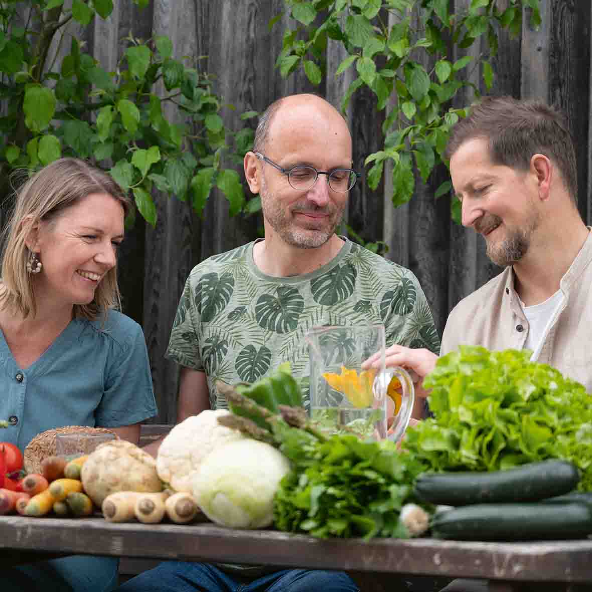 Drei Personen stehen hinter einem Brett auf dem viel Gemüse liegt