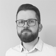 Portrait of a man with glasses, a beard, and short hair wearing a white button-up shirt against a plain background.