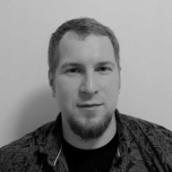 Portrait of a man with short hair, a beard, and a patterned shirt against a plain light background.