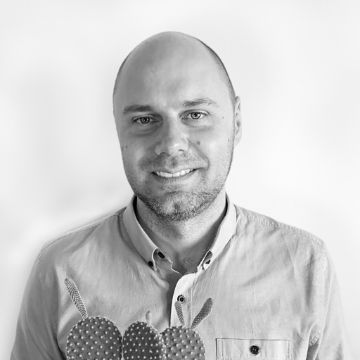 Smiling bald man wearing a buttoned shirt with textured round patches on the chest pocket area.