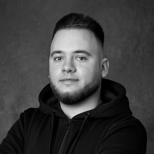 Black and white portrait of a young man with short hair and a beard wearing a hoodie against a plain background.