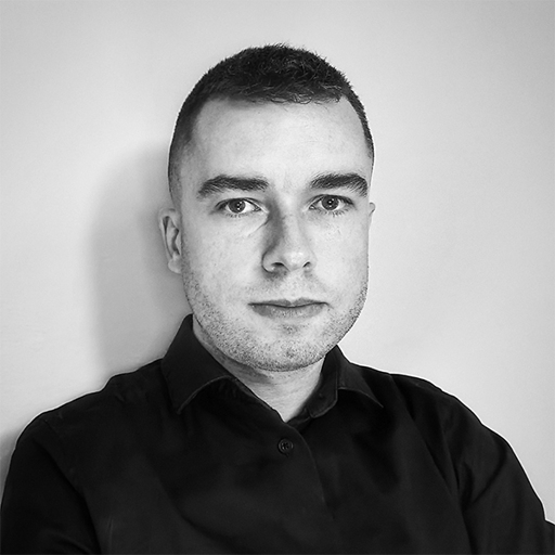 Black and white portrait of a man with short hair wearing a dark collared shirt, looking directly at the camera.
