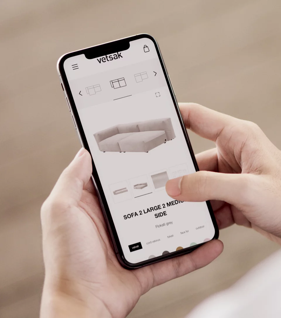 Person holding smartphone displaying an online shop page for a grey sectional sofa labeled 'SOFA 2 LARGE 2 MEDIUM SIDE.'