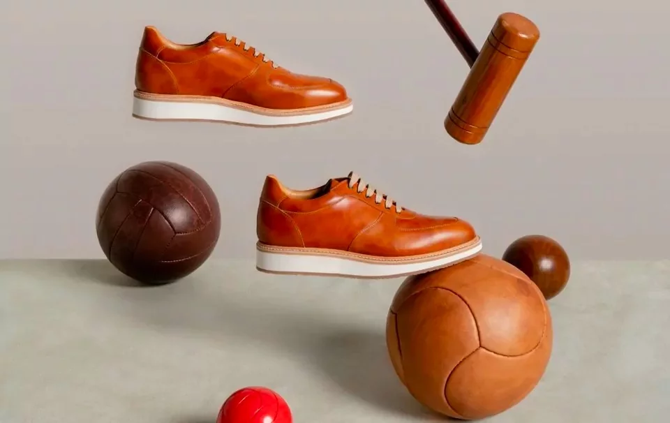 Brown leather sneakers floating among vintage leather balls and a wooden croquet mallet.
